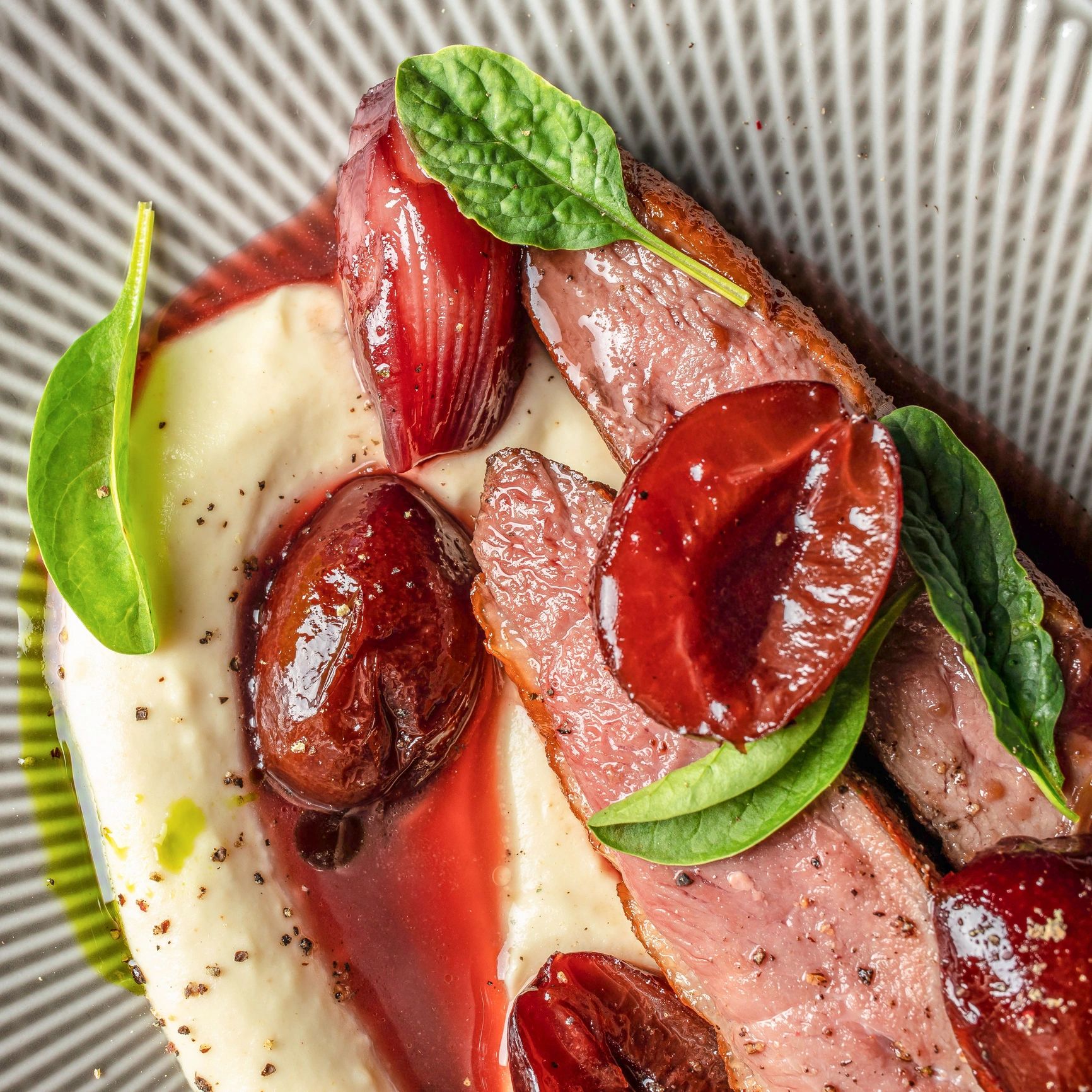 Gourmet duck breast plated with sauce, greens, and mashed potatoes