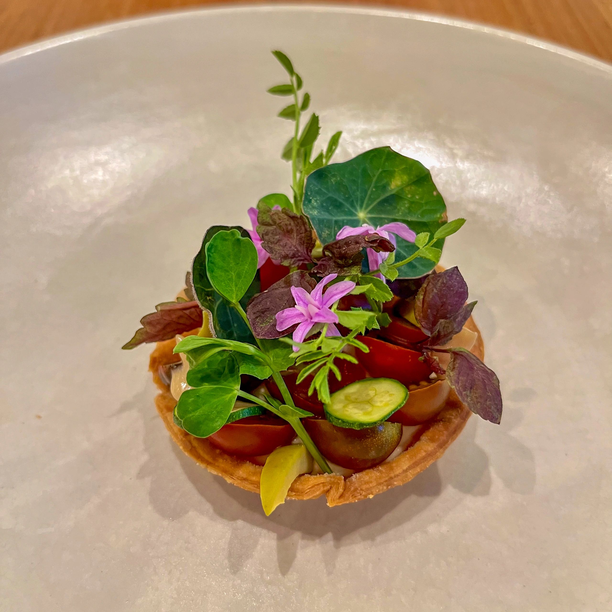 Gourmet savory tartlet plated with tomatoes, cucumbers, edible flowers, and microgreens
